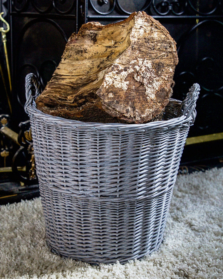 Stylish grey round wicker log basket with durable handles, designed for elegant firewood storage, displayed against a simple backdrop to highlight its modern weave and chic appearance.