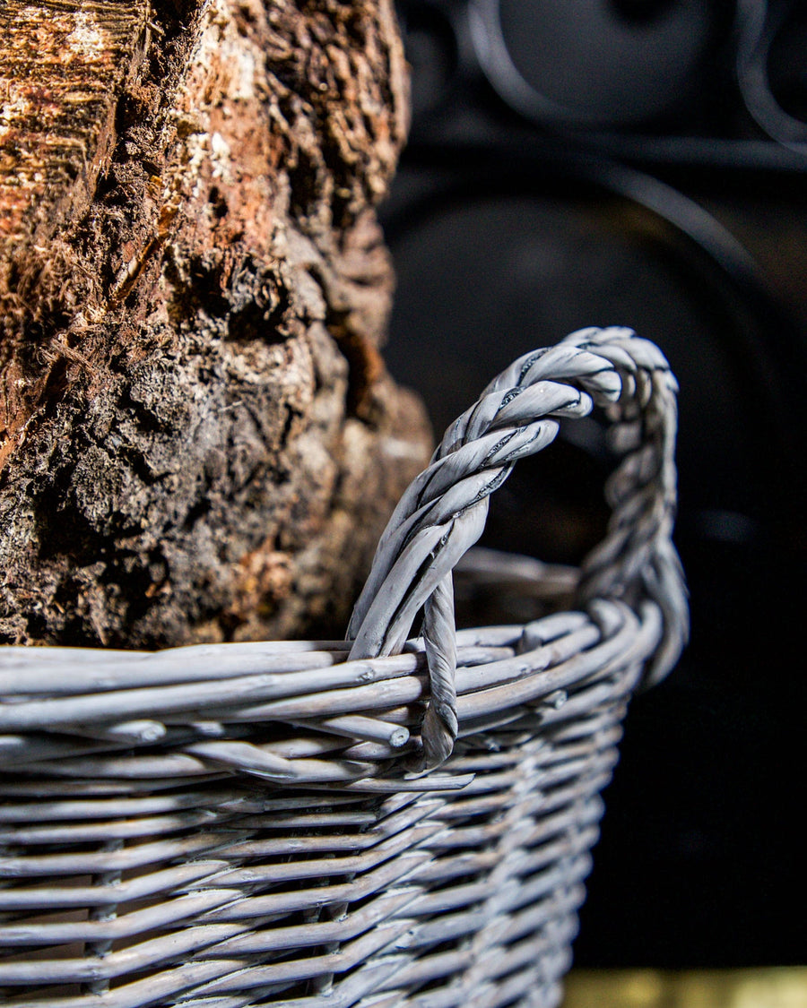 Stylish grey round wicker log basket with durable handles, designed for elegant firewood storage, displayed against a simple backdrop to highlight its modern weave and chic appearance.